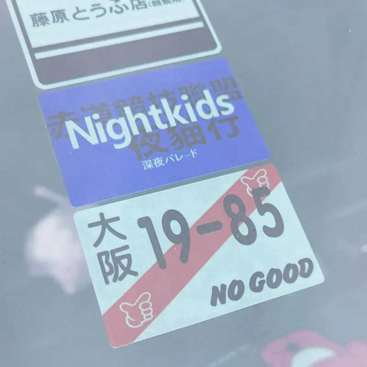 Close-up of Nightkids-style and Osaka 19-85-style static cling decals on glass