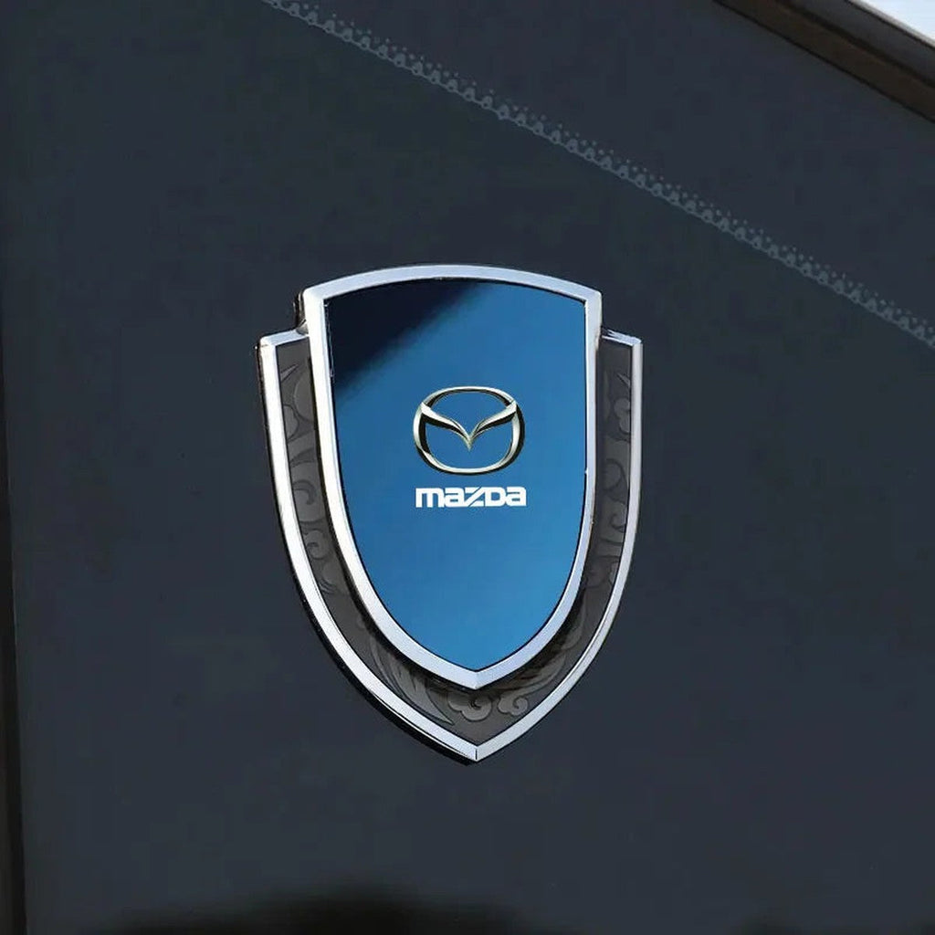 Blue and chrome Mazda-style 3D metal shield emblem on a dark car body