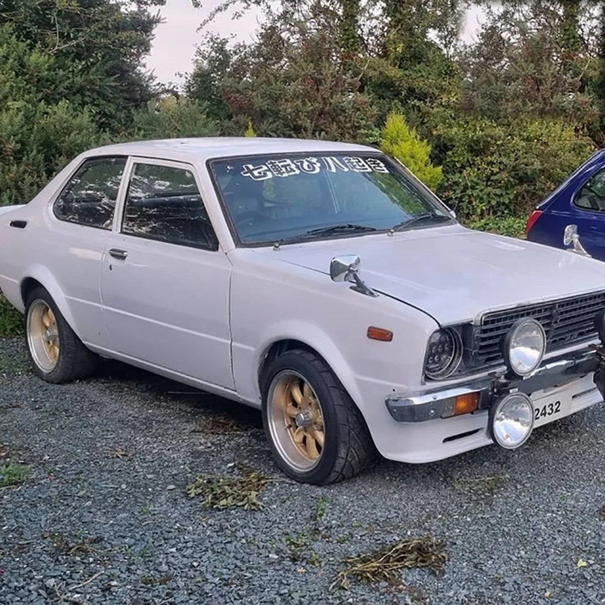 White classic Corolla coupe with a Never Give Up kanji banner on the windshield