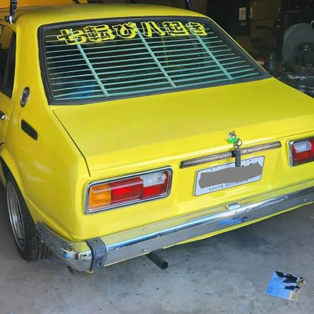 Never Give Up kanji decal on the rear window of a yellow classic hatchback