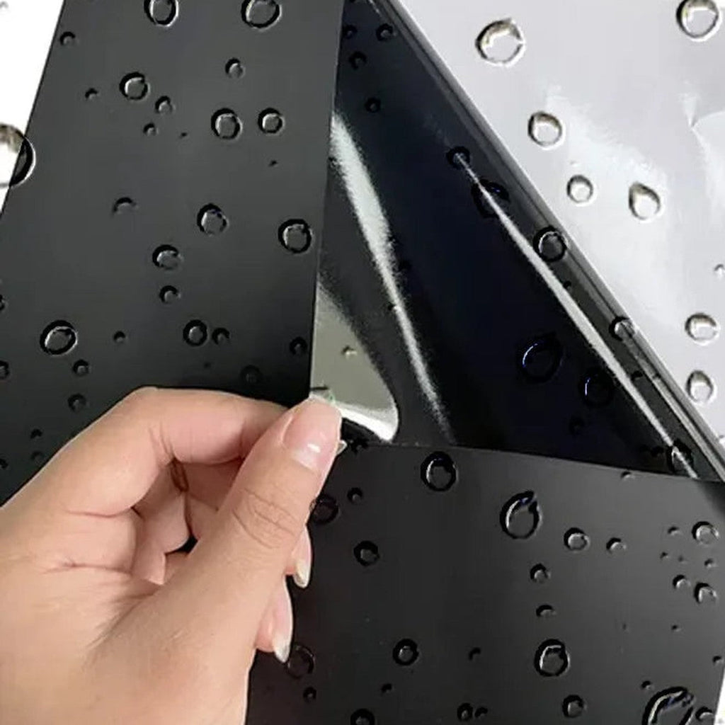 Hand peeling a black vinyl sun strip sheet with water beads on the surface